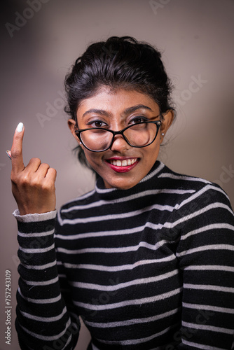 A woman with glasses is smiling and pointing her finger. She is wearing a striped sweater and has red lipstick on
