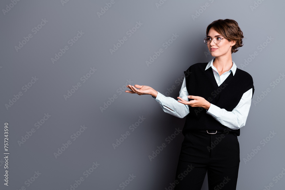 Photo of clever charming lady partner dressed black vest eyewear looking showing arms empty space isolated grey color background Photo of clever charming lady partner dressed black vest eyewear looking showing arms empty space isolated grey color background
