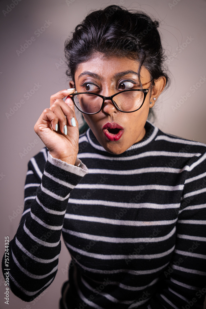 A woman with glasses is wearing a striped shirt and has her mouth open. She is surprised or shocked