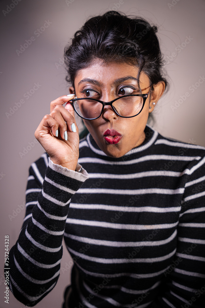 A woman wearing glasses and a striped shirt is looking at the camera with a surprised expression. Concept of curiosity and intrigue, as the woman's gaze seems to be focused on something specific