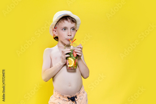 Child boy drinking mojito while standing on yelolow background. Children and summer concept