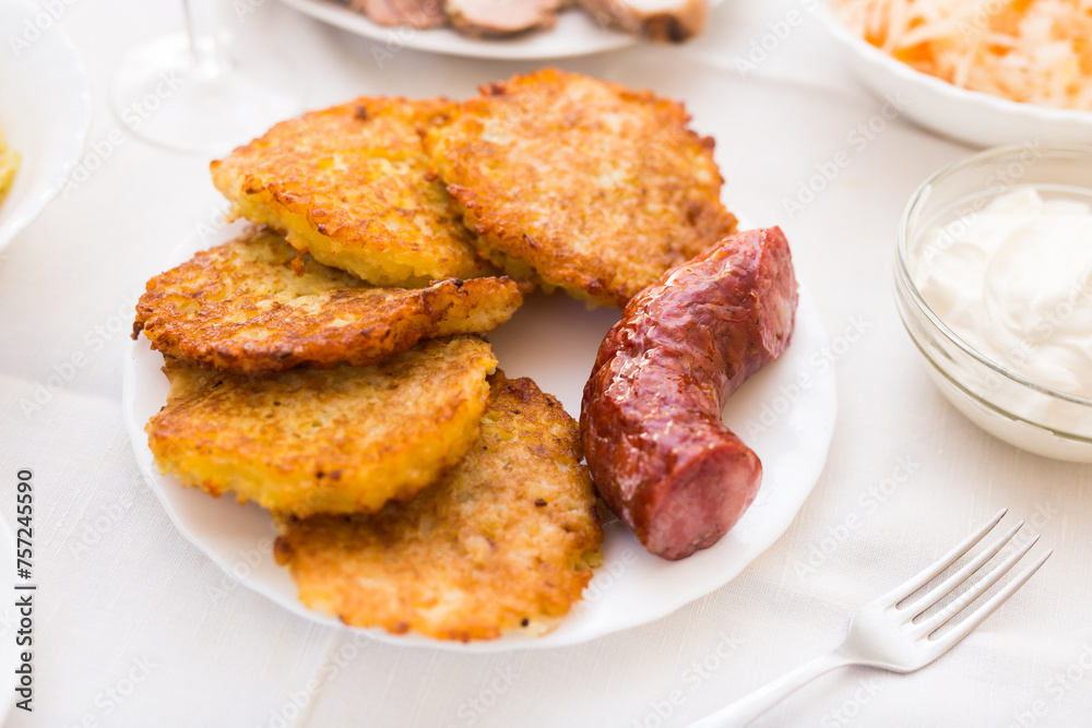 Fried grated potato pancakes with fried sausage on white plate