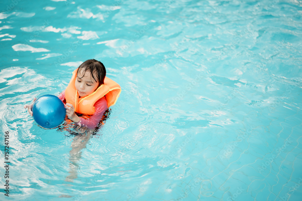 A little asian girl in swimming in the pool. Cute girl playing in outdoor swimming pool on a hot summer day. Kids learn to swim.