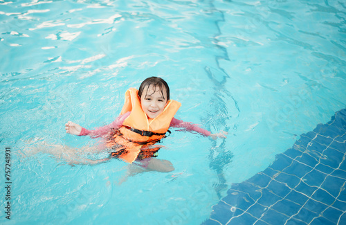 A little asian girl in swimming in the pool. Cute girl playing in outdoor swimming pool on a hot summer day. Kids learn to swim.