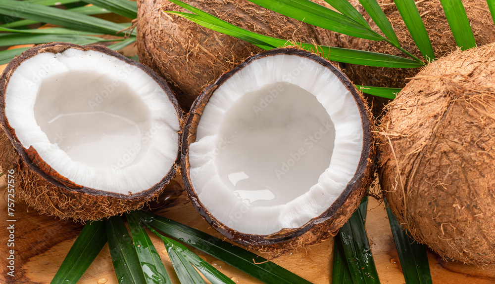 Fresh opened coconuts along with whole coconuts and coconut leaves on a wooden table. Fresh opened coconuts along with whole coconuts and coconut leaves on a wooden table.
