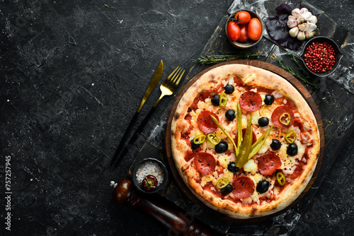 Delicious homemade pizza with pepperoni and vegetables. Home delivery of food. On a black stone background.