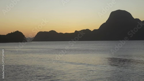 A tropical evening after sunset. The ocean water undulates calmly. Glare on the surface. A picturesque mountain range against the sky, highlighted in orange. Philippines. Palawan Island. El Nido