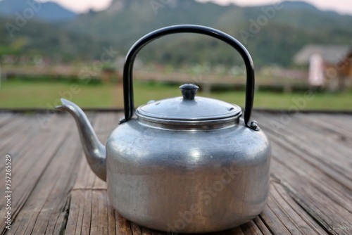 Traditional old-fashioned kettle made from aluminum, handle made from bakelite painted black, used for boiling drinking water. Vintage or retro. Old kettle placed on bamboo table on natural background photo
