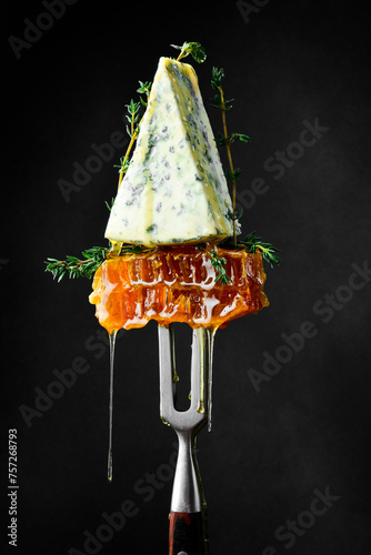 A piece of blue cheese with honeycombs. On a fork. Aged elite cheese.