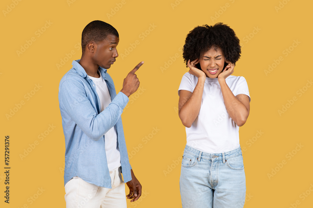 An upset young woman covering her ears while a young man points at her An upset young woman covering her ears while a young man points at her