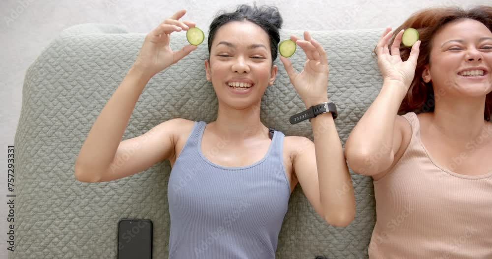 Two female friends are lying down with slices of cucumber on their eyes, smiling joyfully Two female friends are lying down with slices of cucumber on their eyes, smiling joyfully