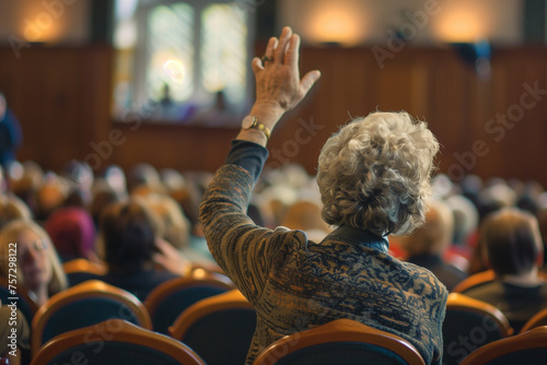senior woman with hand up to talk at local town hall meeting, from back view © Ricky