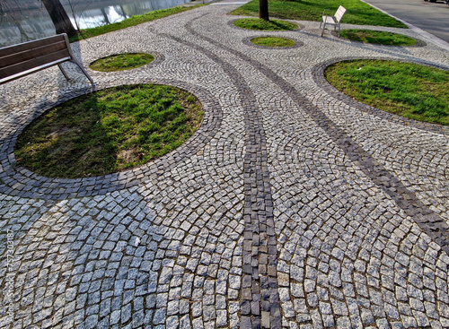 stepping stones lead to a small circular lawn in the middle of a flower bed. sitting on a bent bench made of red tropical wood. automatic sprinkler hoses on the surface of the soil, snake, upper view