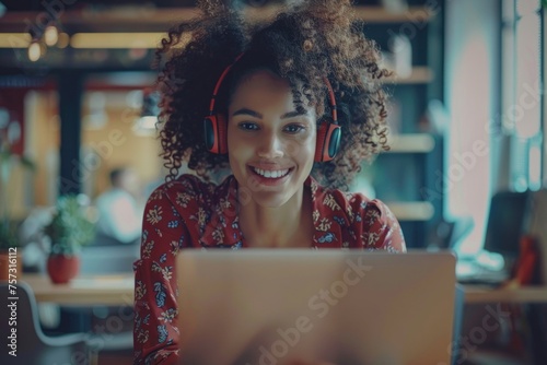 beautiful woman inside the office works with a laptop,a businesswoman in headphones listens music, podcasts, audio books and training course. Worker smiling, with curly hair and red shirt,GenerativeAI photo