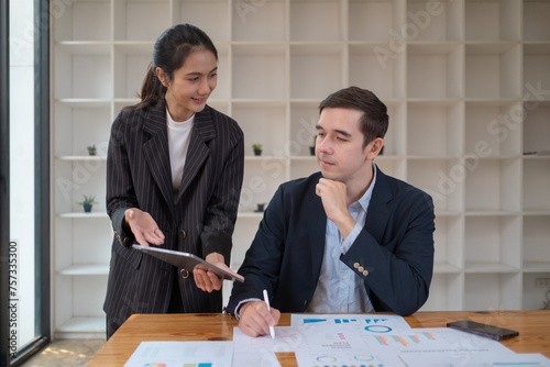 Two business people using a laptop ipad togerher in an office, a man and a women analyzing documents stat at office photo