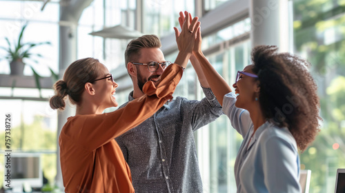 Colleagues are giving each other a high five in an office setting, with big smiles on their faces, indicating a celebration or success.