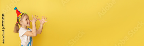 Banner. Funny kid clown against yellow background. Happy child playing with festive decor. Birthday and 1 April Fool's day concept