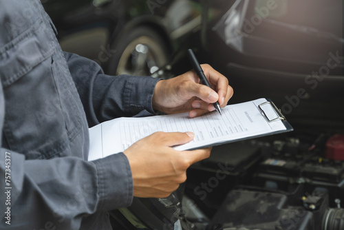 Auto check up and car service shop concept. Mechanic writing job checklist to clipboard to estimate repair quotation to client at workshop garage. © Pormezz