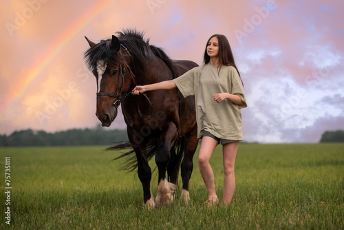 girl is walking a horse in a field with a rainbow in the background