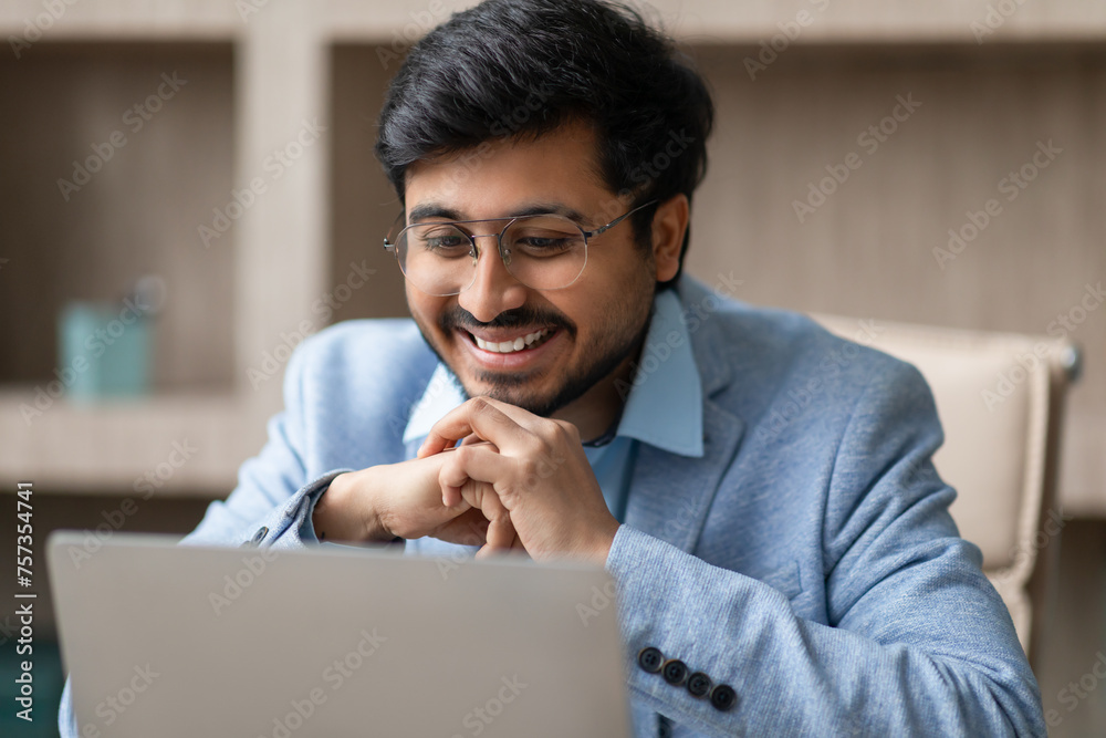 Hindu professional businessman wearing eyeglasses looking at laptop in office - obrazy, fototapety, plakaty 