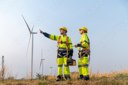 Engineer surveyor and manager wearing uniform walking holding box inspection and tablet work in wind turbine farms rotation to electricity, alternative renewable energy for clean power energy concept.