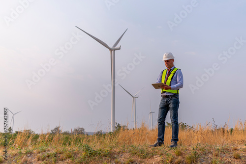 Engineer manager wearing uniform inspection work in wind turbine farms rotation to generate electricity energy. Green ecological power energy generation wind sustainable energy concept.