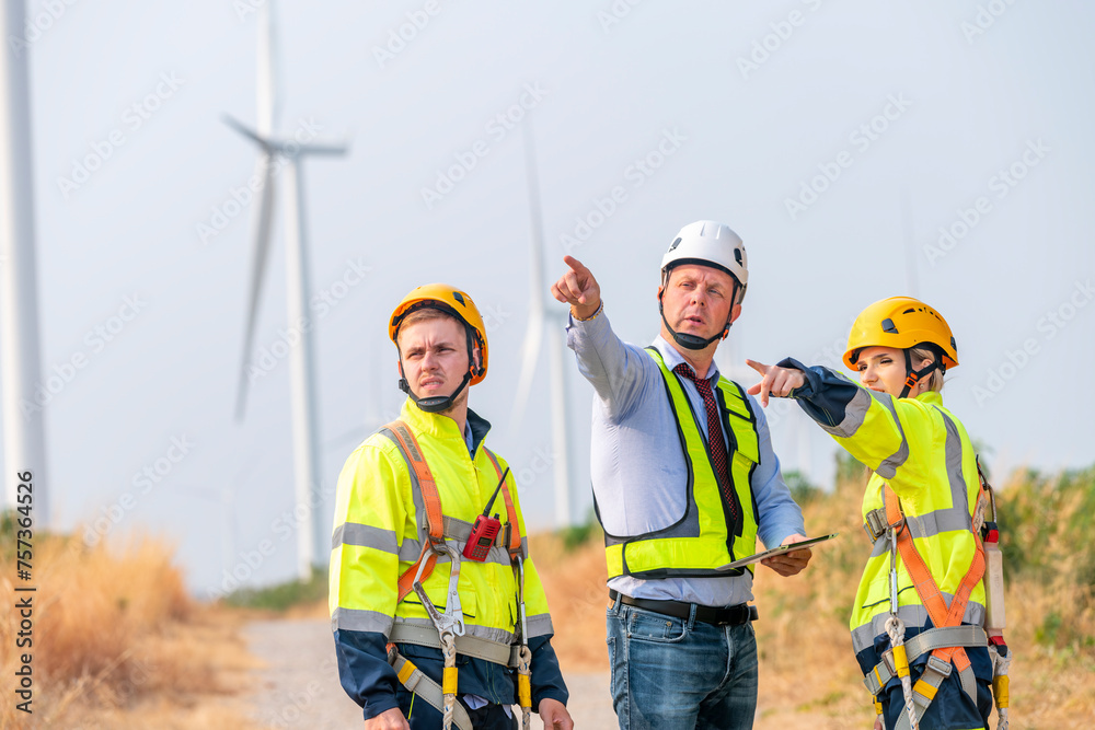 Engineer surveyor and manager wearing uniform walking holding box inspection and tablet work in wind turbine farms rotation to electricity, alternative renewable energy for clean power energy concept. Engineer surveyor and manager wearing uniform walking holding box inspection and tablet work in wind turbine farms rotation to electricity, alternative renewable energy for clean power energy concept.