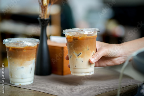 hand of woman holding a take-out iced coffee on wooden table at cafe