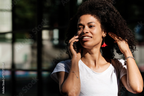 Black woman talking by phone in street.