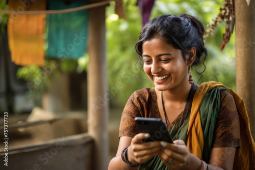 Smiling Indian woman texting on a smartphone while sitting in the courtyard of her house.