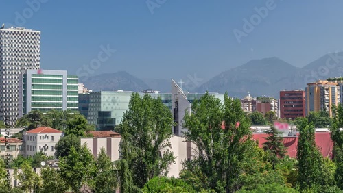 Cityscape over Tirana with its colorful apartment buildings and skyscrapers timelapse, Tirana, Albania. Aerial view from viewpoint of pyramid with green trees and mountains photo