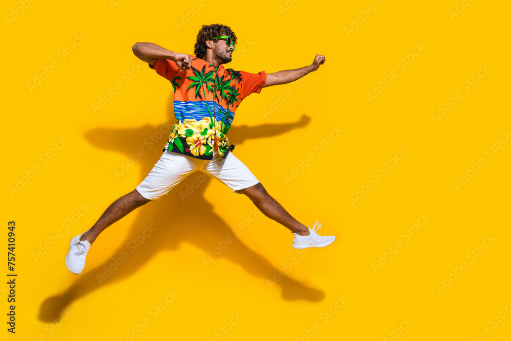 Full size photo of active man dressed print shirt flying clenching fists look at discount empty space isolated on yellow color background