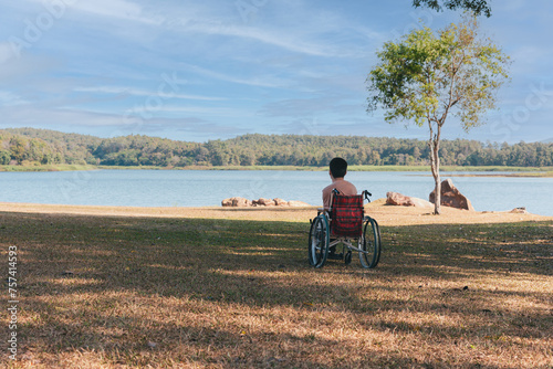 Back of young boy sitting on wheelchair looking at beautiful nature park, Traveling using a wheel chair to learn about the world without limits, Good mental health and travel concept.