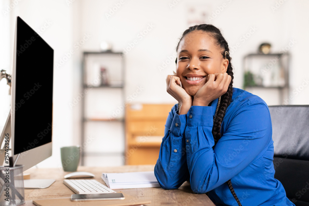 Contented black lady with braids at her computer desk at home Contented black lady with braids at her computer desk at home