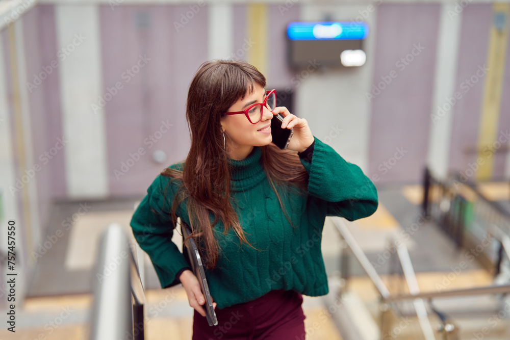 Fototapeta premium busy young professional woman talking on the cell phone leaving the subway