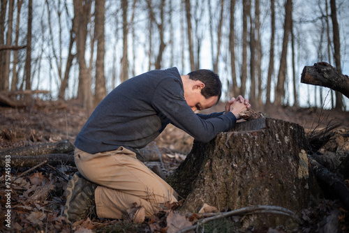 Man kneeling to pray with folded hands on tree stump in the forest