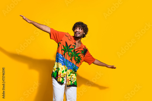 Portrait of impressed guy wear hawaii print shirt arms like wings look at proposition empty space isolated on yellow color background