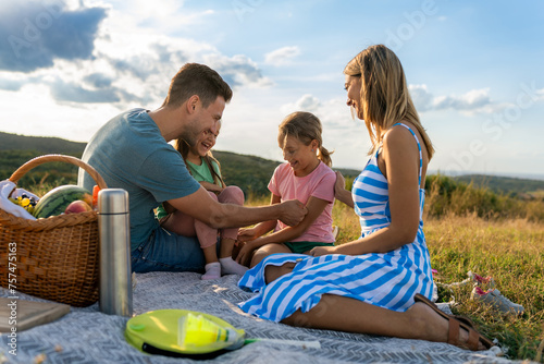 The father holds his daughter in his lap while the mother and older daughter sit on the blanket, talking about their day © DusanJelicic