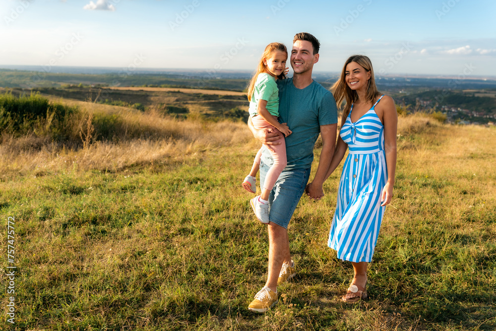 A young couple, a father and a mother with their daughter, are walking in a field, the father is holding the daughter on his shoulder A young couple, a father and a mother with their daughter, are walking in a field, the father is holding the daughter on his shoulder