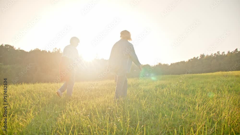 Camera view from behind of three women walking up hill with green grass. Sun shining very bright. People living actively. Females walking and jumping together through wide field and smiling. Camera view from behind of three women walking up hill with green grass. Sun shining very bright. People living actively. Females walking and jumping together through wide field and smiling.