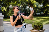 stylish woman with short haircut walking in street with coffee wearing black top, jeans and sunglasses accessories