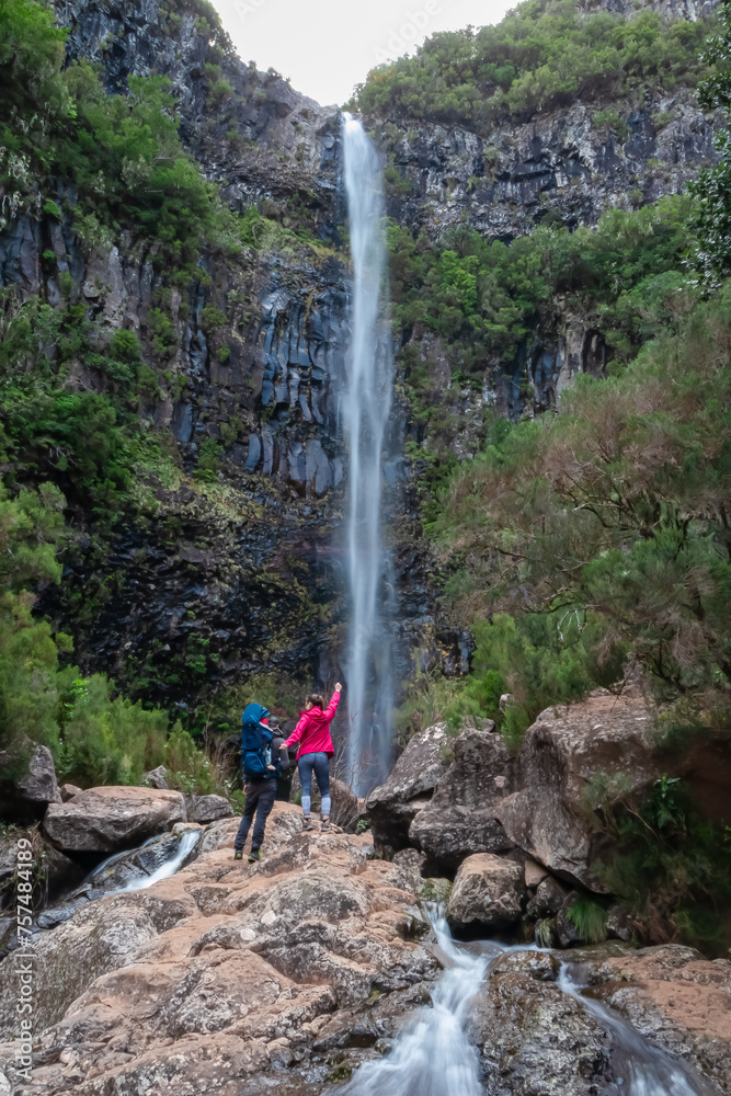 Family with baby carrier looking at majestic waterfall Cascata Risco along idyllic Levada walk 25 fountains in evergreen subtropical Laurissilva forest of Rabacal, Madeira island, Portugal, Europe