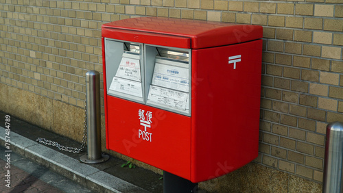 Red mail box in front of brick wall on Japanese street, text means post.