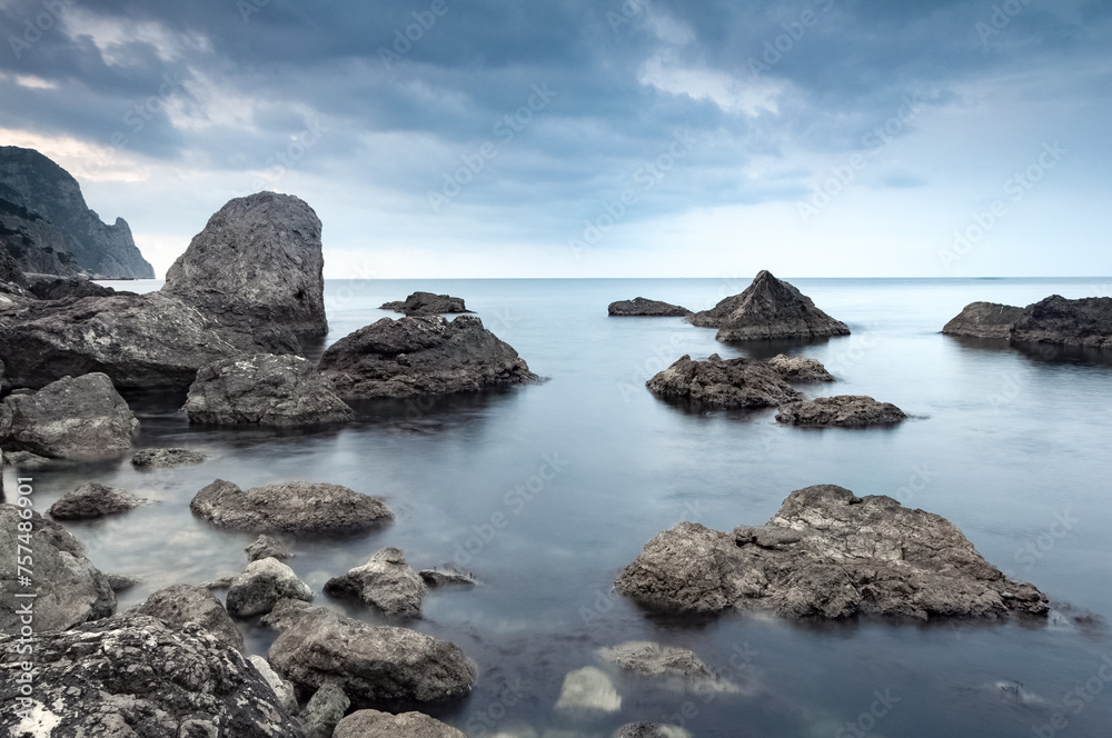 Calm sea. Summer morning. The clouds is reflecting on the water. Landscape with gray and brown stones in the sea. Monochrome scene. 