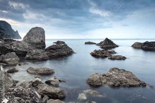 Calm sea. Summer morning. The clouds is reflecting on the water. Landscape with gray and brown stones in the sea. Monochrome scene.  © Vitalii_Mamchuk