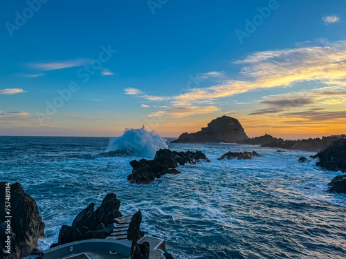 Panoramic sunset view of volcanic rock formation Ilheu Mole in coastal town Porto Moniz, Madeira island, Portugal, Europe. Rugged coastline of majestic Atlantic Ocean. Waves smashing against shoreline photo