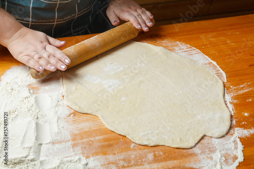 A woman's hand rolls out dough with a rolling pin on a table sprinkled with flour