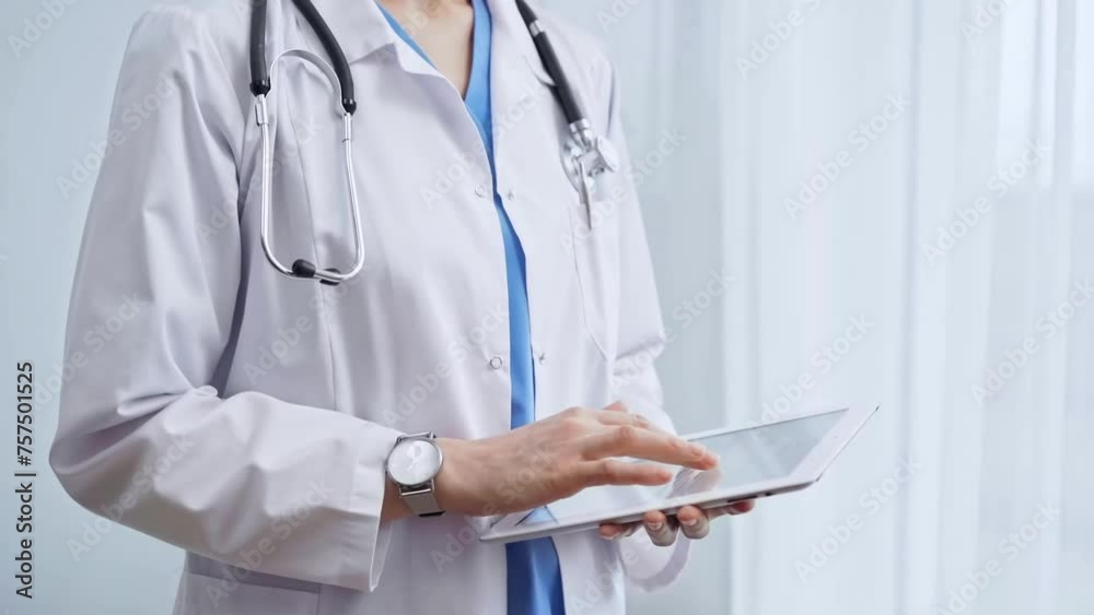 Female doctor using digital tablet in clinic. Healthcare professional with a stethoscope around her neck operating a touchscreen computer while standing on the glass background. Medicine and