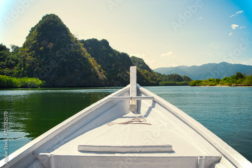 Prow of a white boat heading towards the lush greenery and limestone cliffs of Langkawi UNESCO-listed Geopark in Malaysia photo