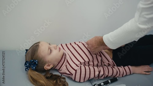 A pediatrician examines a little girl patient lying on her back on an examination couch. The doctor palpation the girl's abdomen. The child smiles during the procedure photo